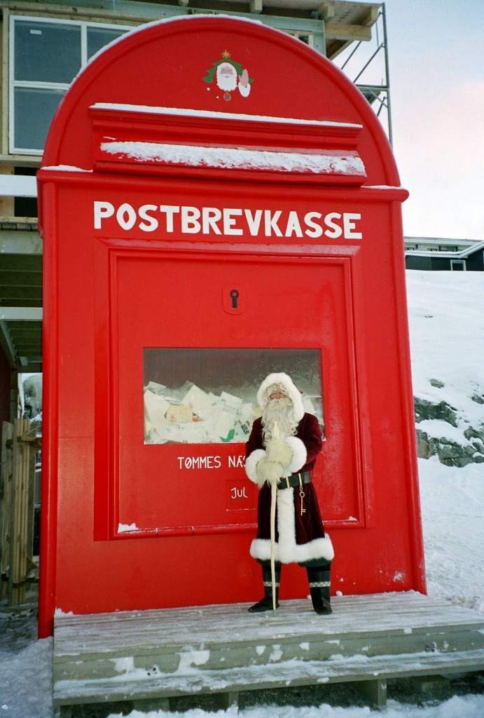 Santa Claus standing in front of a large red mailbox 